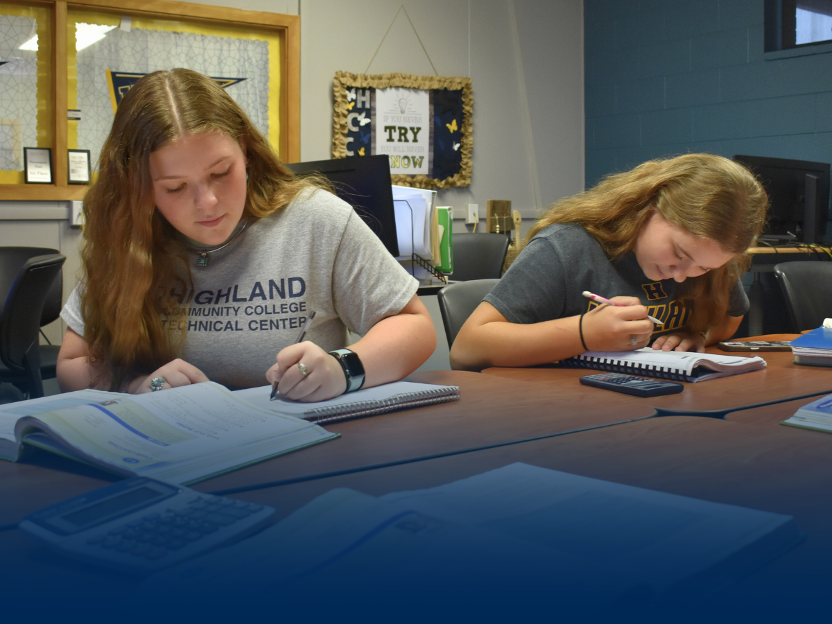 Two students sitting at a desk reviewing a textbook and course work.