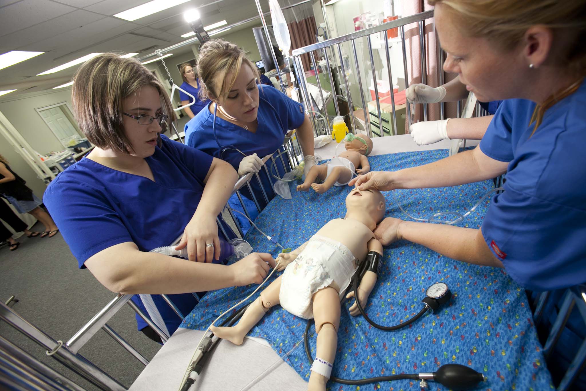 This image shows three nursing students practicing a medical procedure on an infant doll