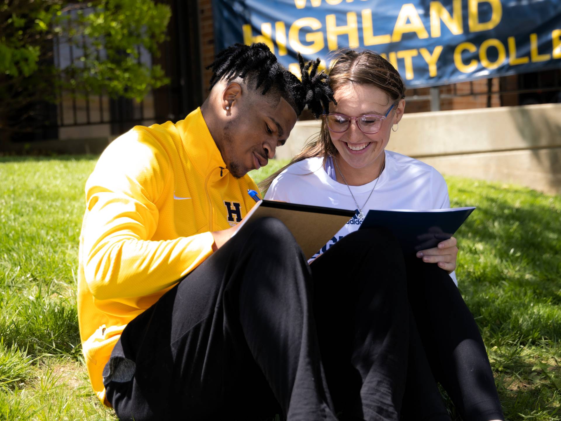 Two students sitting on the lawn taking notes on notepads
