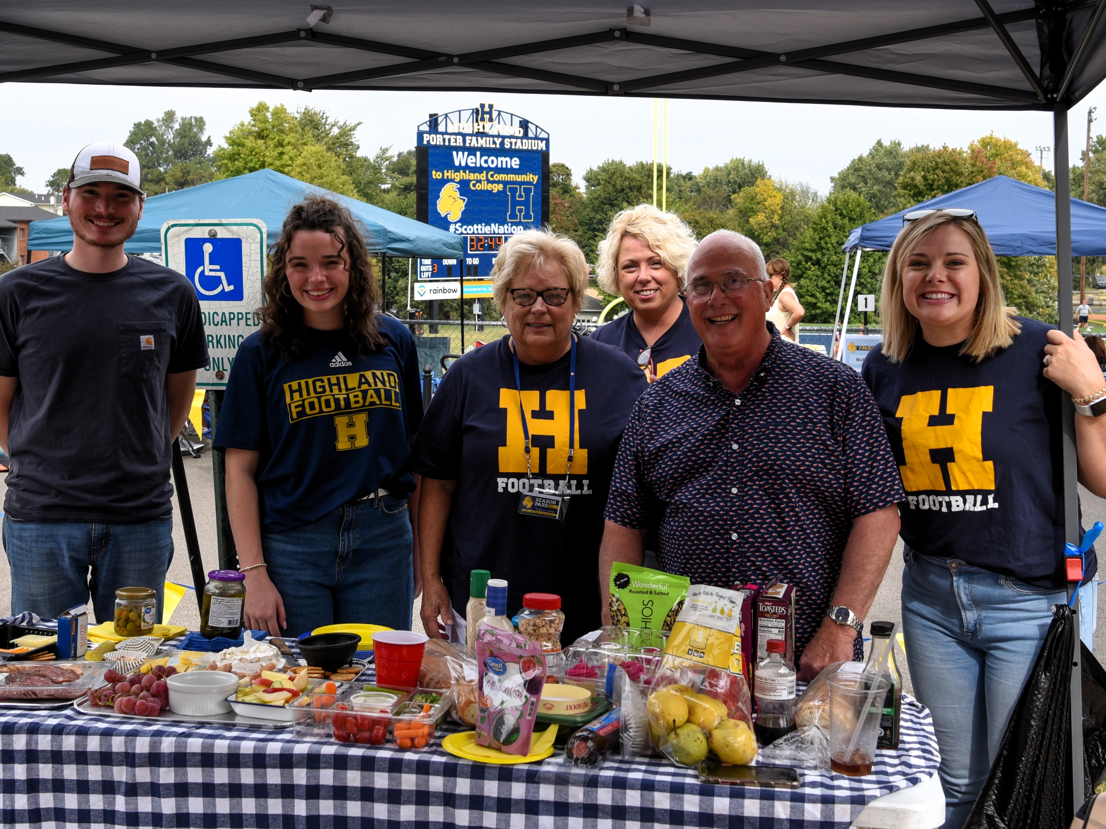 Group of alumni gather together with a table full of food as they tailgate during a football game