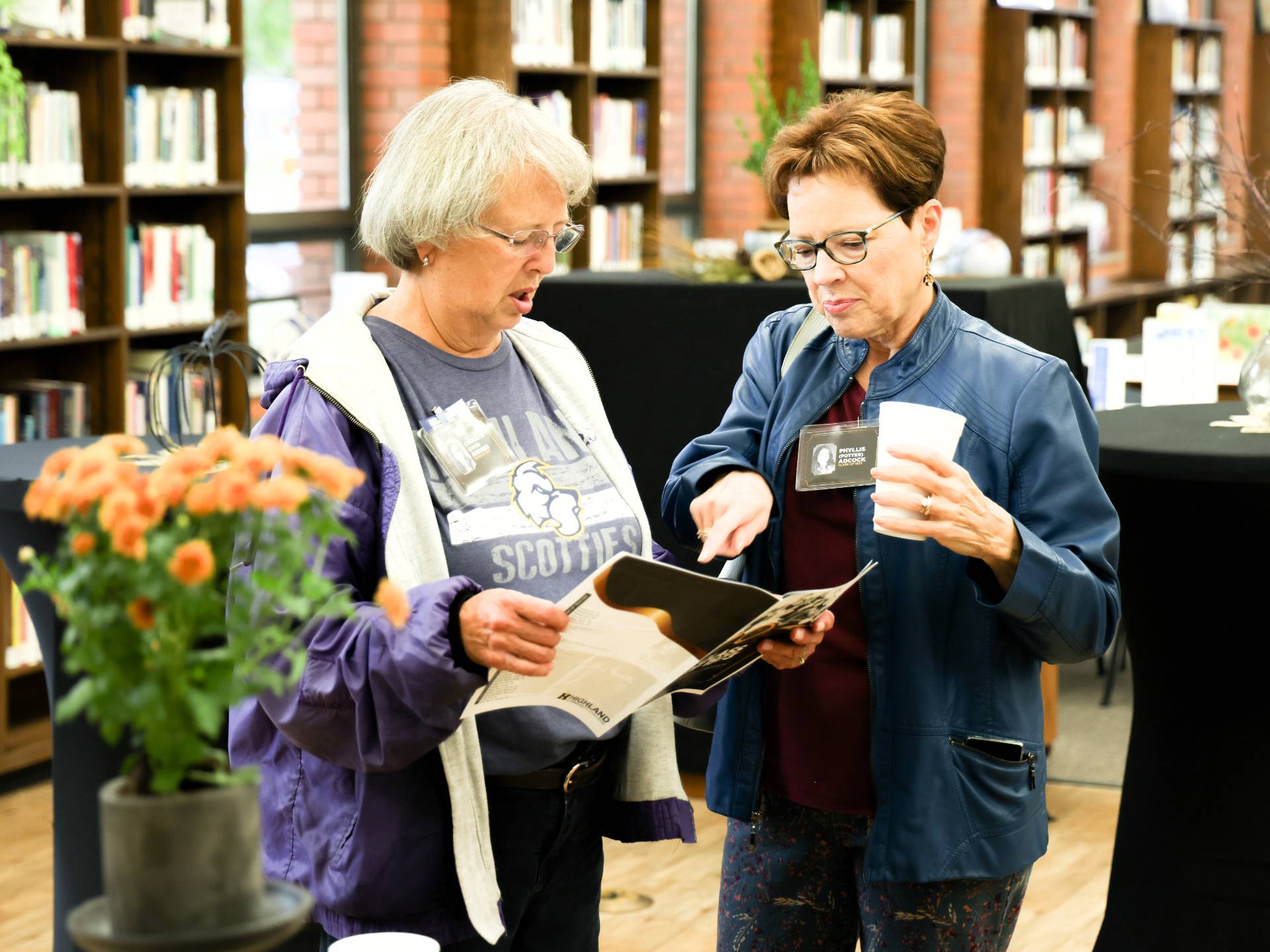 Two alumni are looking at a flyer together at an alumni event hosted in the library.