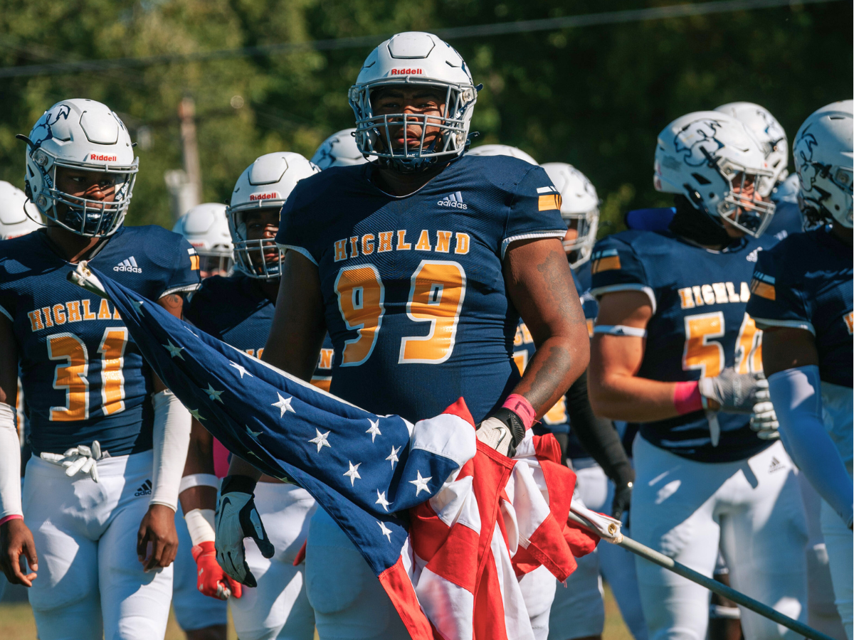 Scottie Football player in uniform holding the American flag with teammates standing behind him.