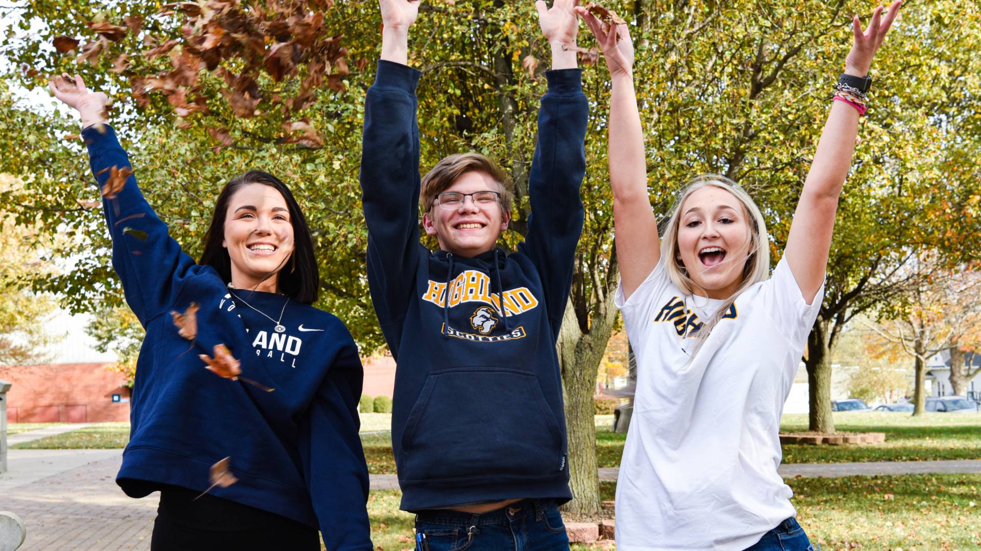 Three students on the lawn, smiling at the camera. They are wearing blue and white sweatshirts with "Highland" on them.