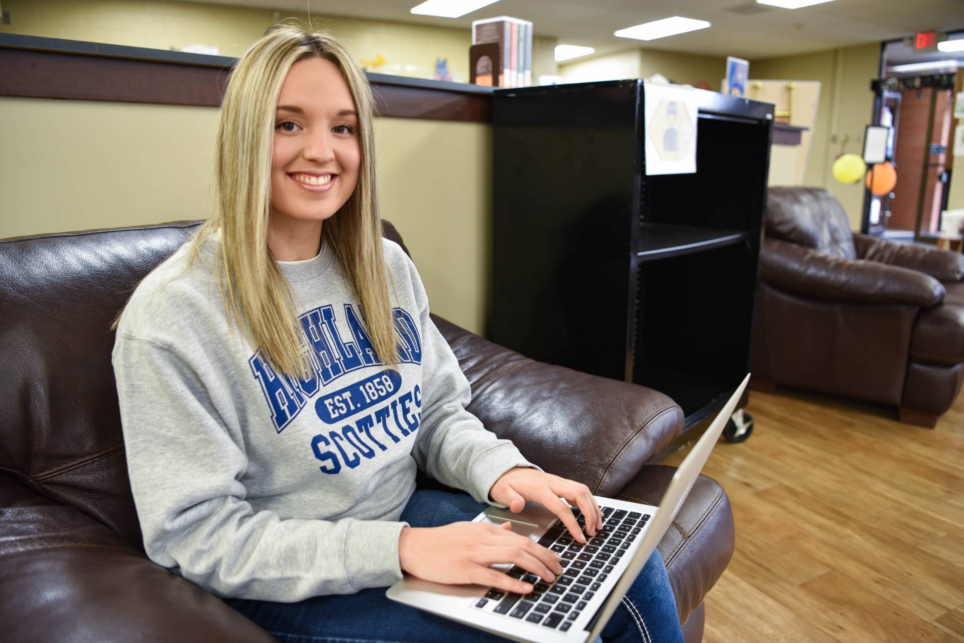 Student using a laptop, smiles at the camera.