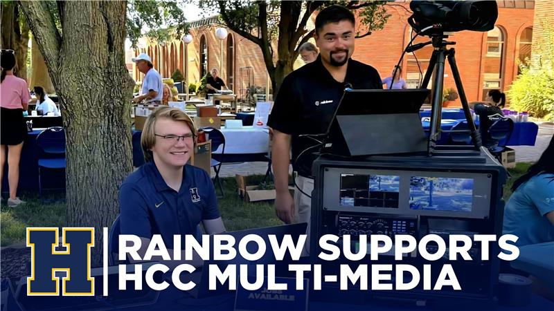 Tanner Holte with Rainbow representative at a tabling event. Banner reads Rainbow supports HCC Multi-Media