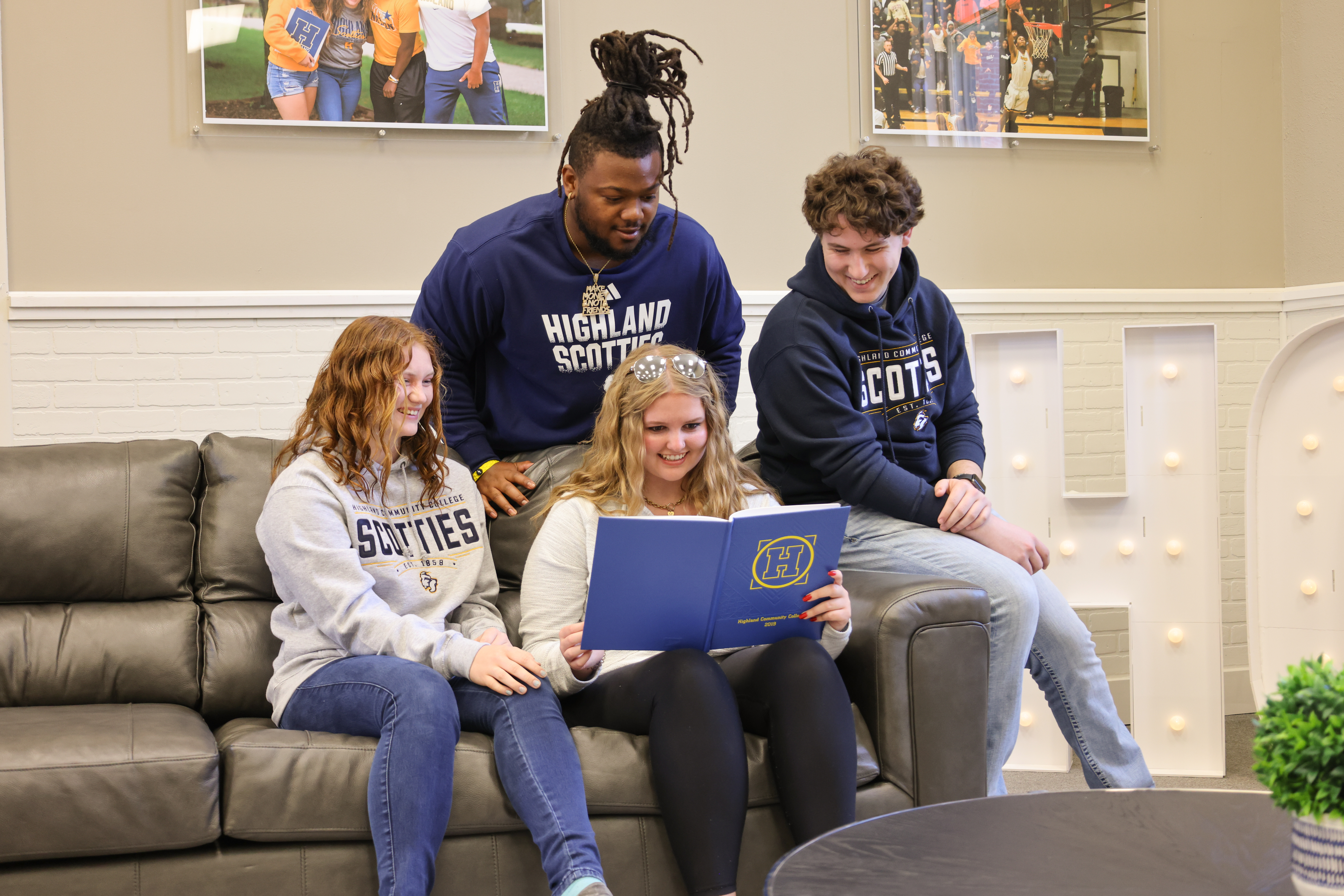 Students sitting together on a couch looking at a yearbook or flyer